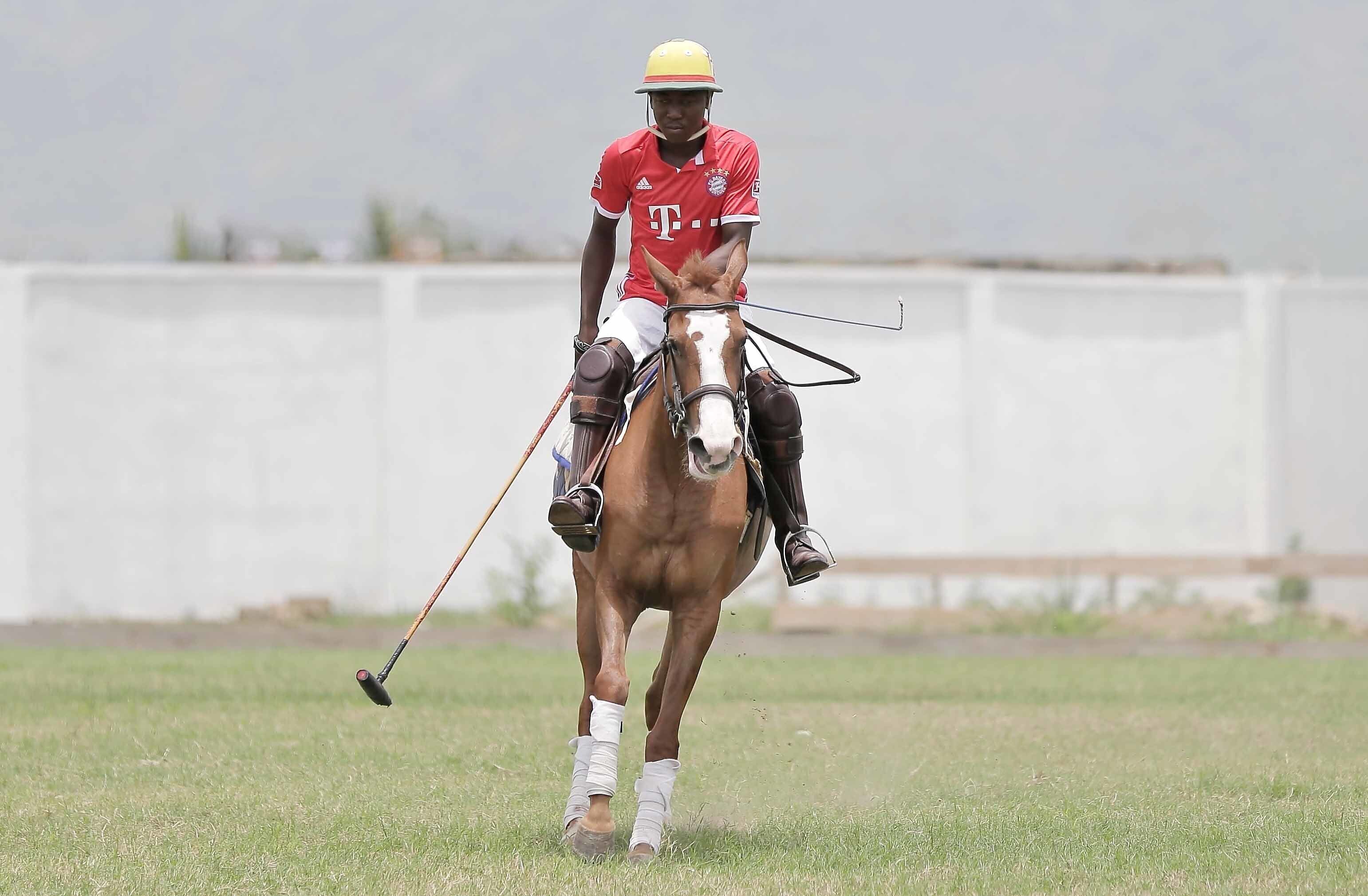 A person riding a horse in a grassy field with a white fence in the background.