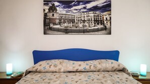A bedroom with a bed, a blue headboard, a floral-patterned pillow, and a framed picture of a historical building on the wall. - A Casa di Frà B&B (Palermo)