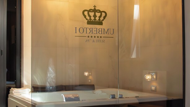 A modern bathroom with a large mirror, a chandelier, and a bed with white bedding. - Umberto Primo Suite e Spa (Naples)