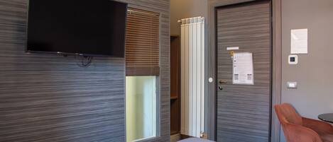 Una habitación de hotel con una cama, un televisor montado en la pared, una puerta con un papel adherido y una silla.
