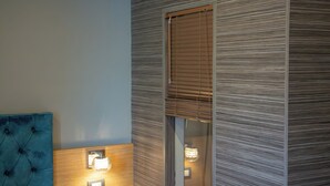 A room with a tufted headboard, a wall-mounted light fixture, and a window with blinds. - Umberto Primo Suite e Spa (Naples)