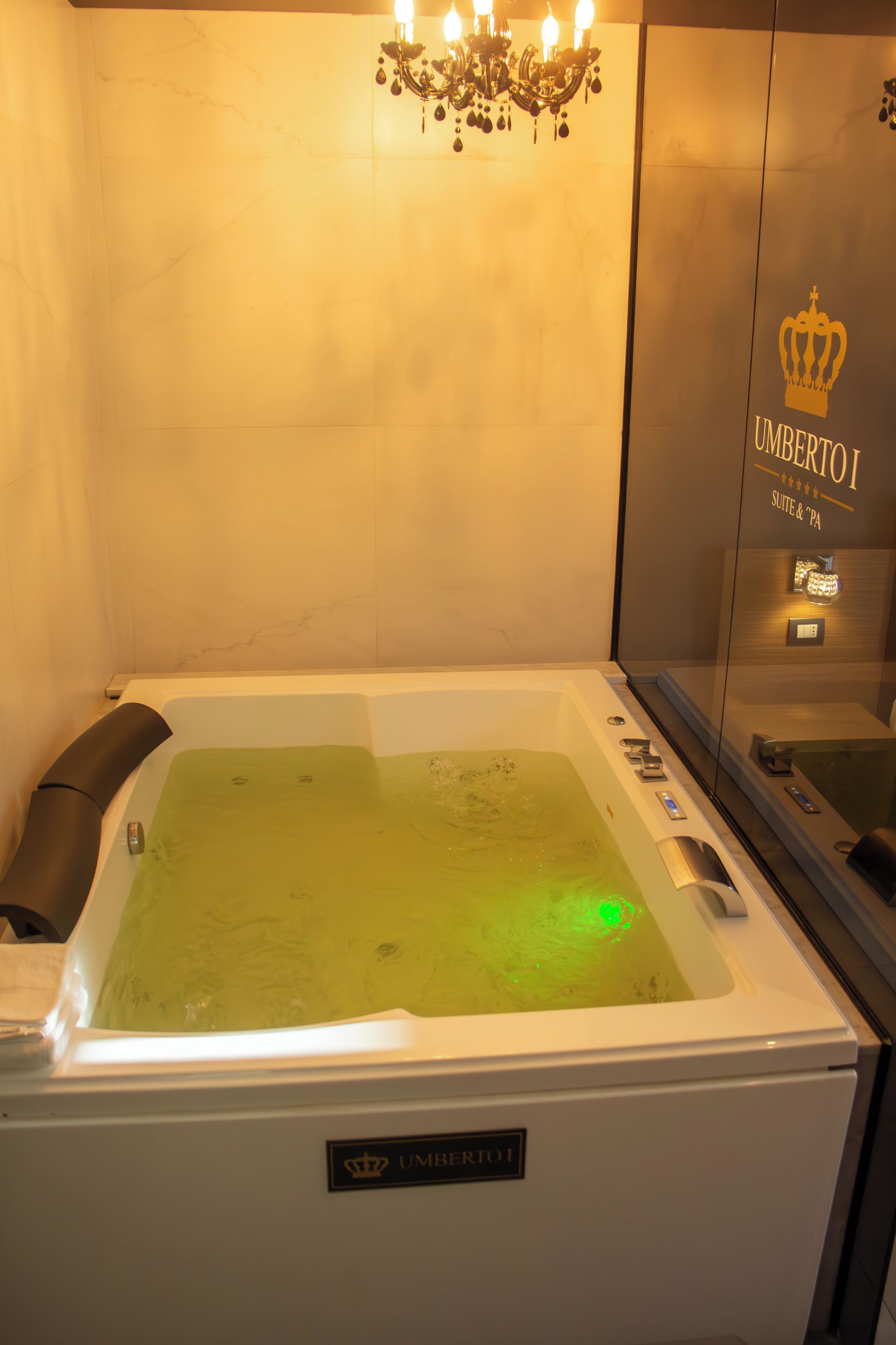 A spa tub with a green light, a chandelier, and a sign reading "UMBERTOI SUITE & SPA".