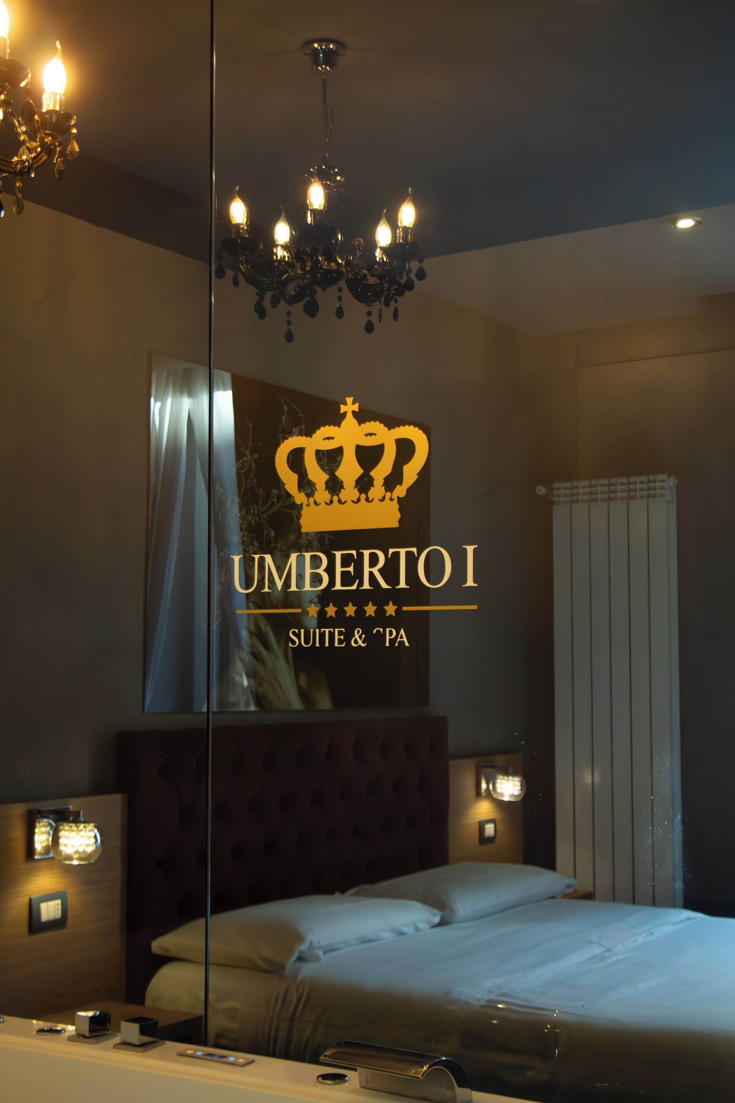 A modern hotel room with a large bed, a chandelier, and a mirror reflecting the room's decor.