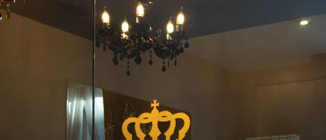 A modern hotel room with a large bed, a chandelier, and a mirror reflecting the room's decor.