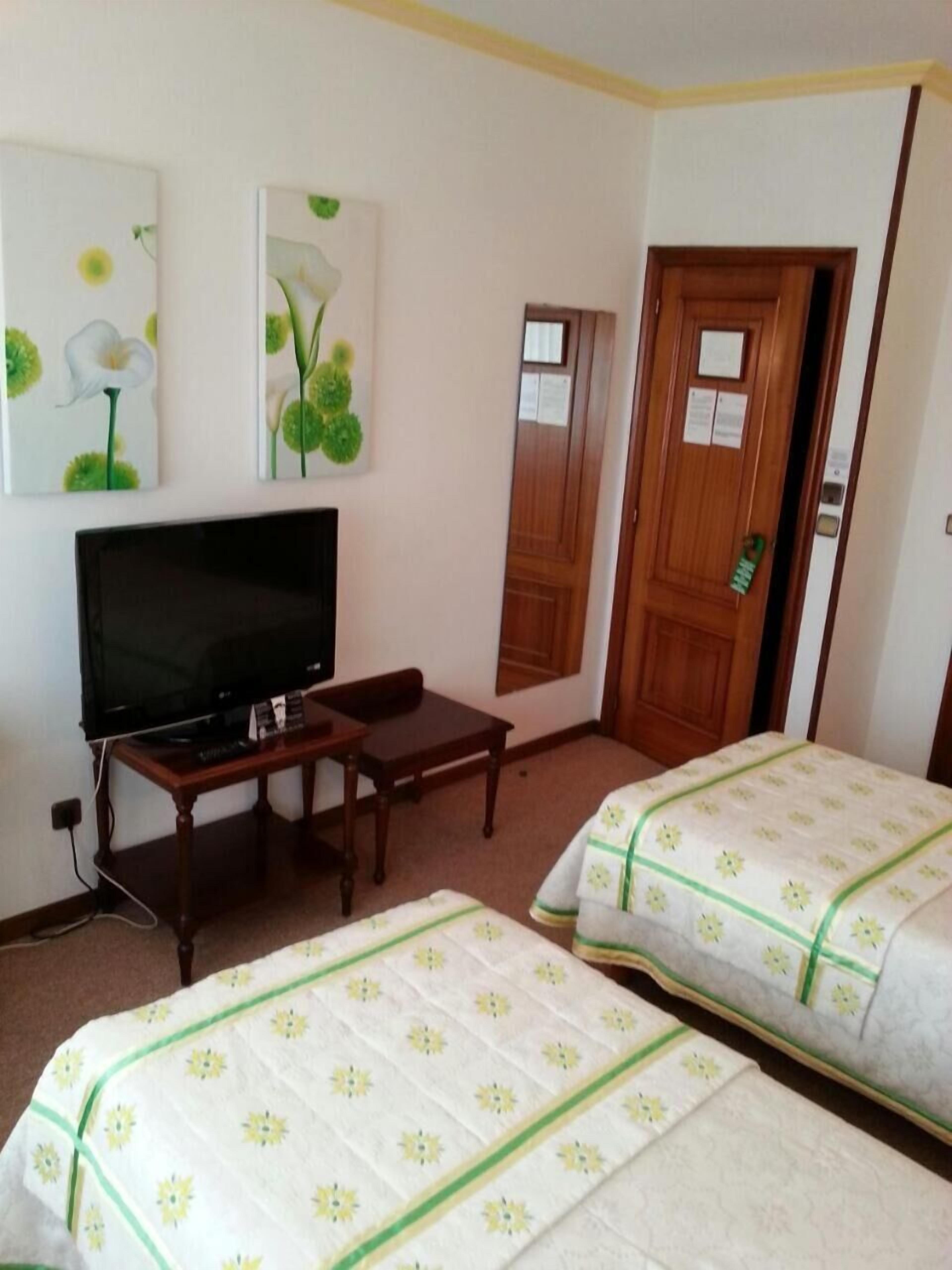 A hotel room with a television, a wooden desk, two beds with floral bedding, and a door with a mirror.