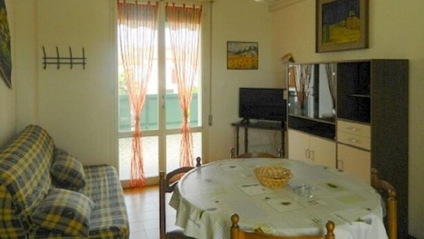 A small, cozy room with a bed, a table with a basket, a TV, and a window with curtains.