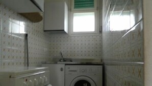 A small laundry room with a washing machine, a dryer, and a window with blinds.
