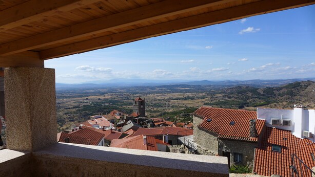 Vista desde un balcón sobre un pueblo con tejados rojos y una torre destacada.