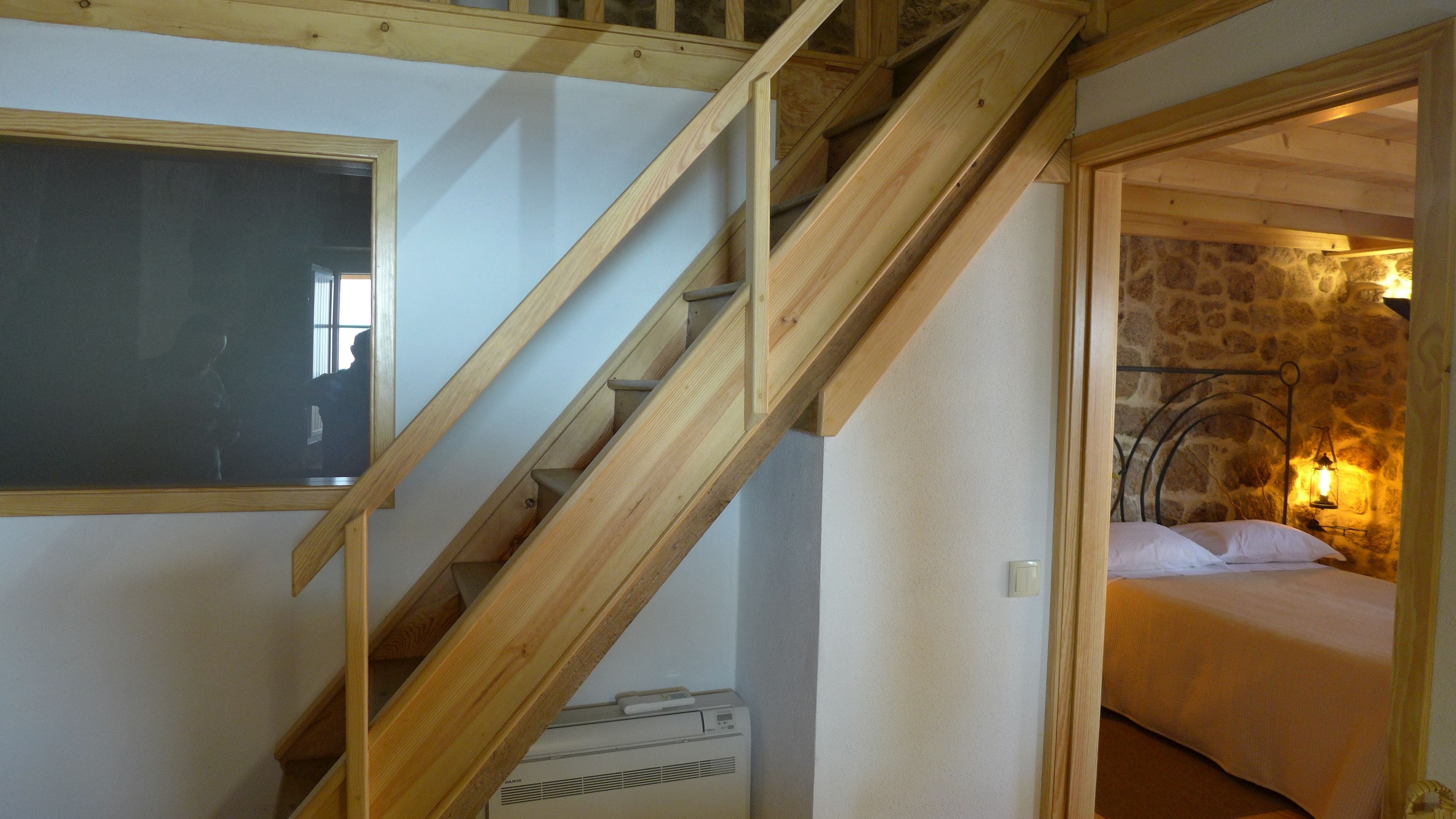 Una escalera conduce a un dormitorio con una pared de piedra y una cama con ropa blanca.