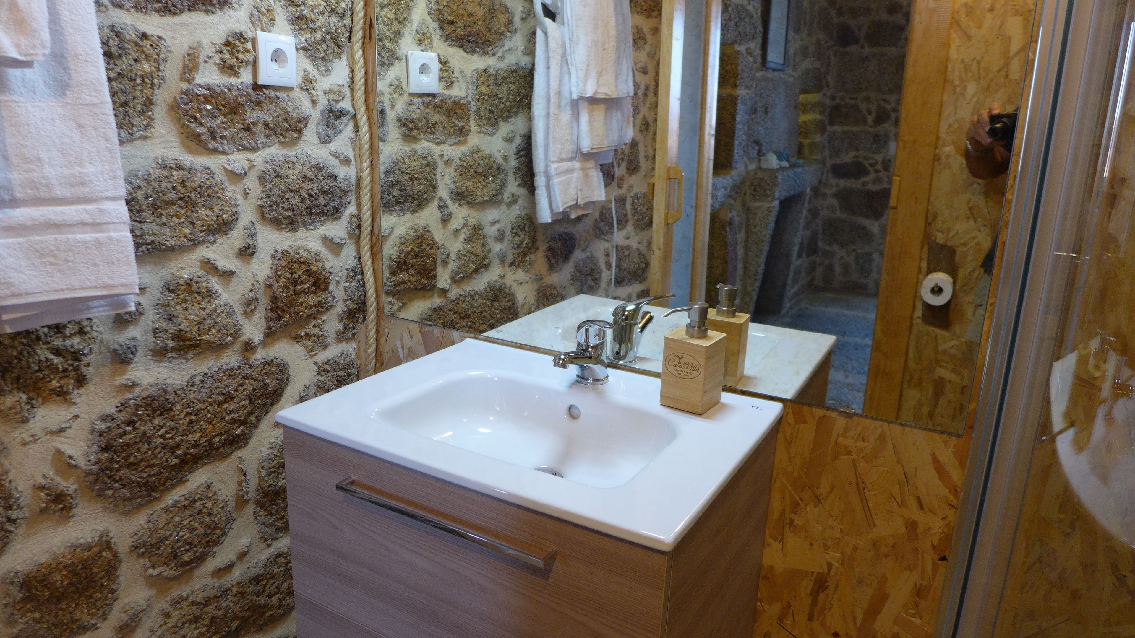 A bathroom with a stone wall, a white sink, a wooden cabinet, and a mirror.