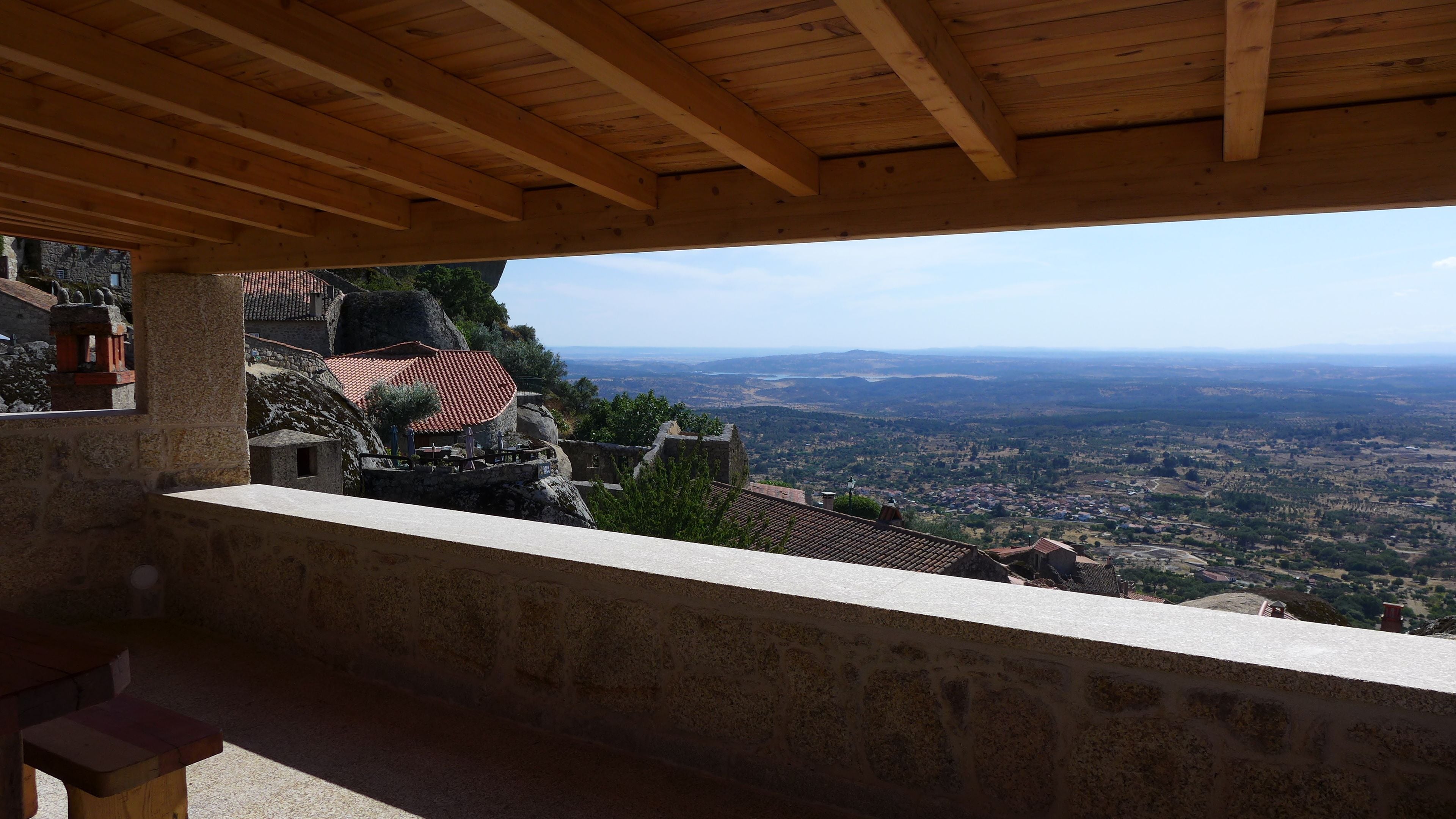 A stone balcony with a wooden ceiling overlooking a valley.