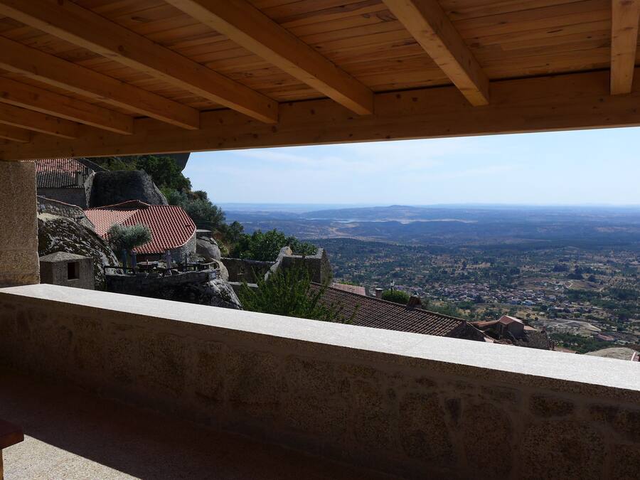 A stone balcony with a wooden ceiling overlooking a valley.