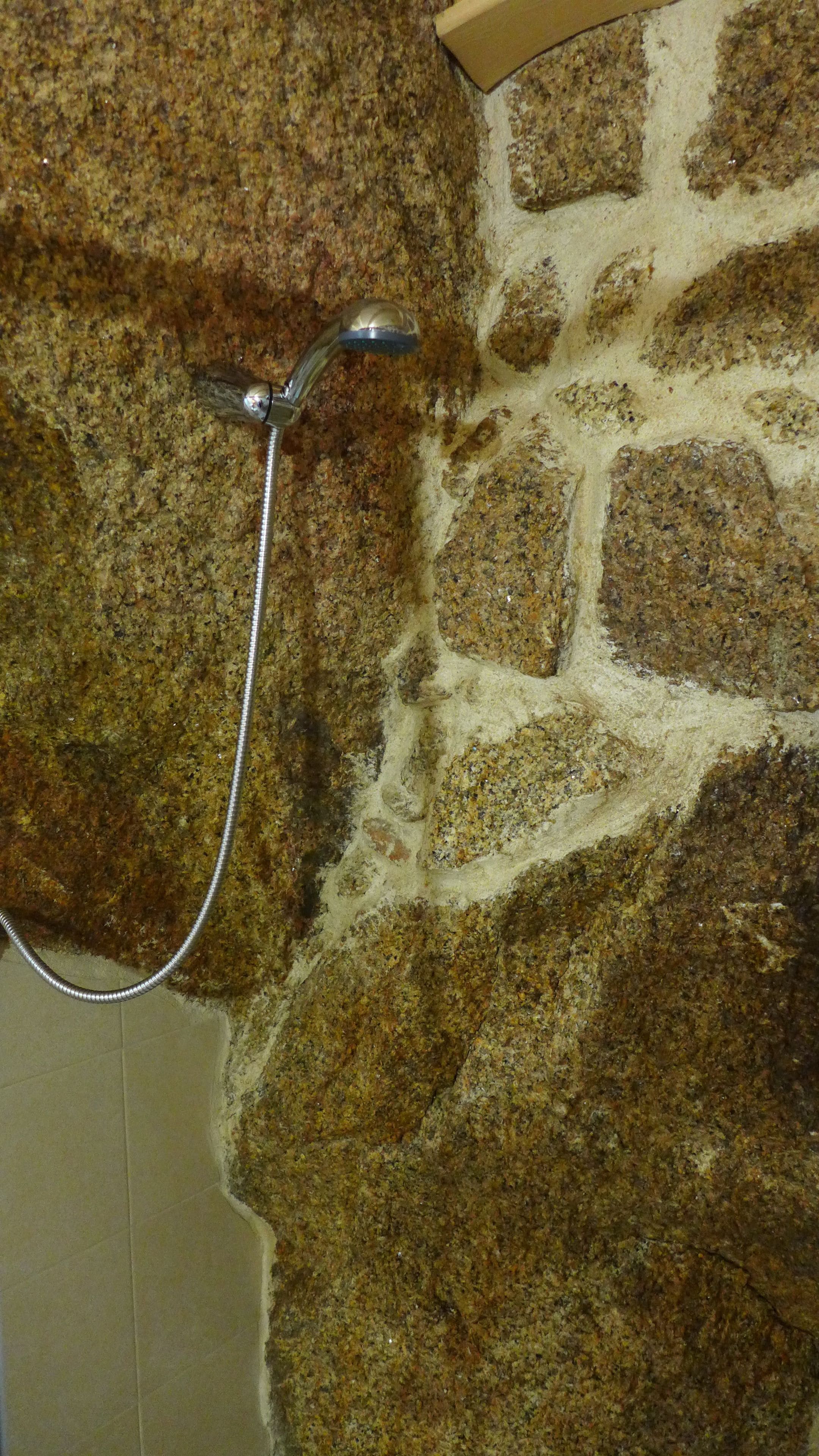 A shower area with a stone wall and a metal shower head.