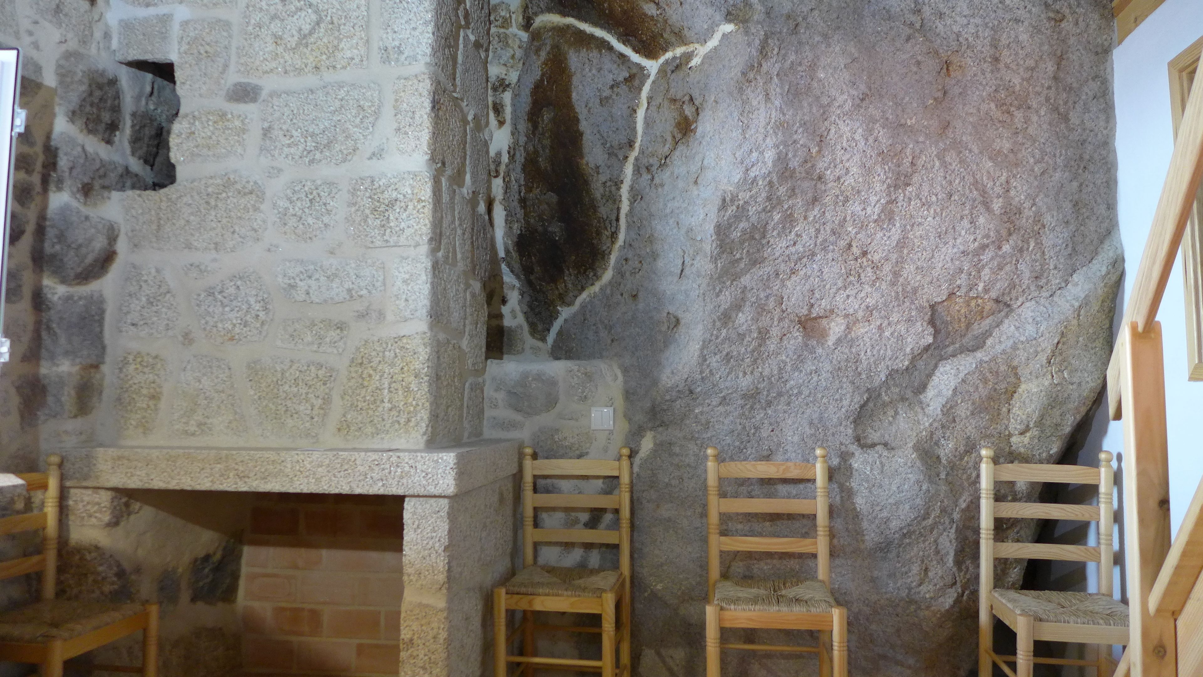 A stone wall with a fireplace, wooden chairs, and a wooden bench.
