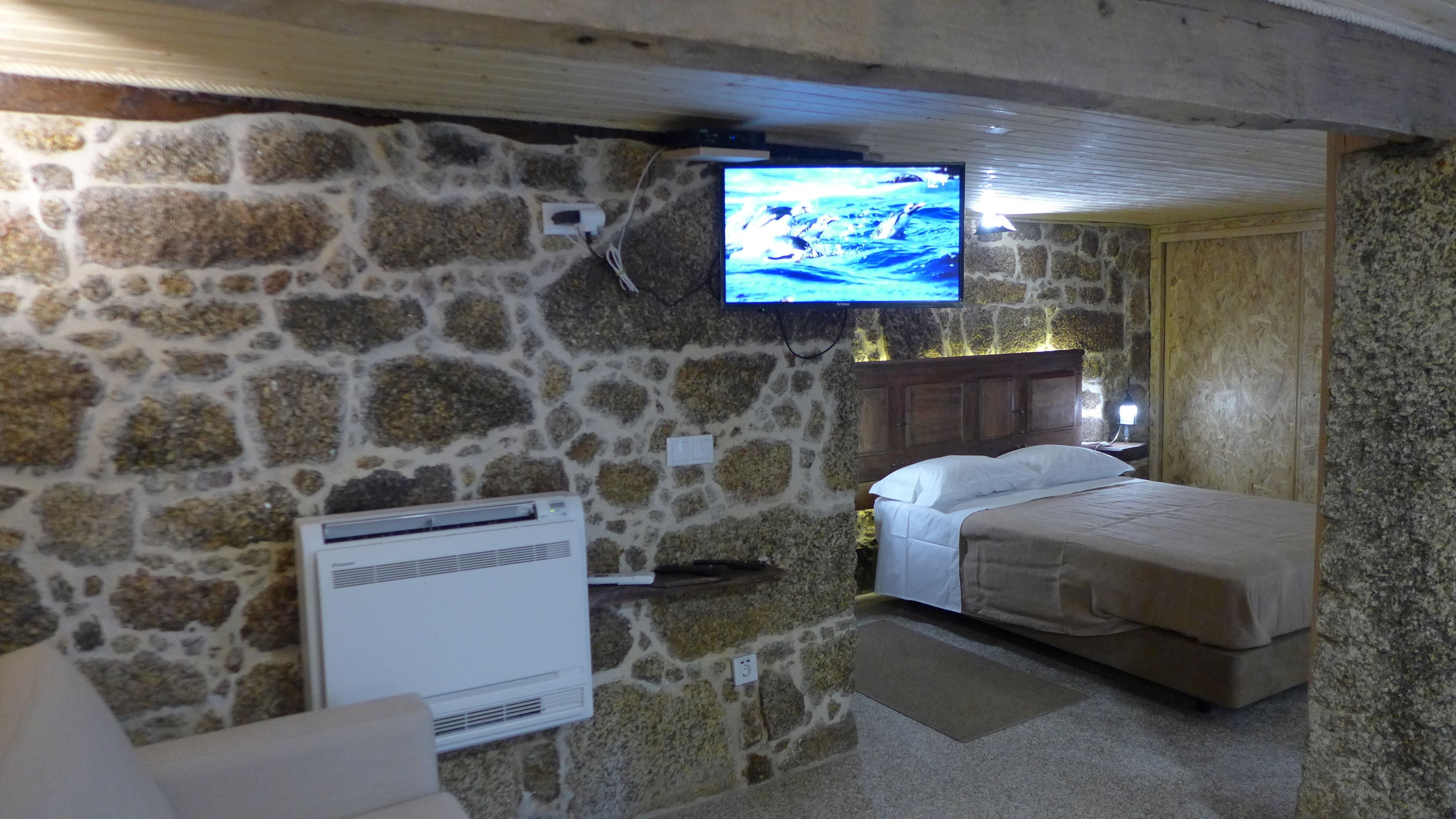 A stone-walled room with a bed, a TV mounted on the wall, and an air conditioning unit.
