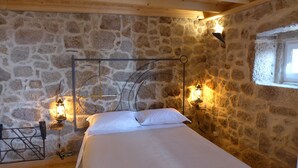 Un dormitorio con paredes de piedra, una cama, dos lámparas fijadas a la pared y una ventana.