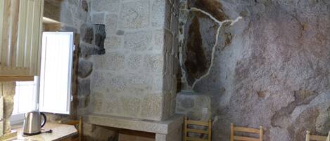 A kitchen with stone walls, a sink, a kettle, and two wooden chairs.