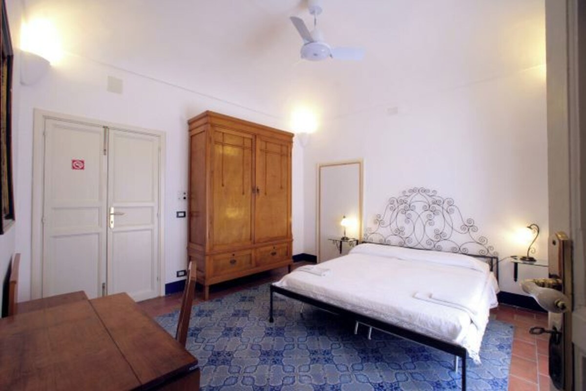 A bedroom with a bed, a wooden wardrobe, a ceiling fan, and a nightstand with a lamp.
