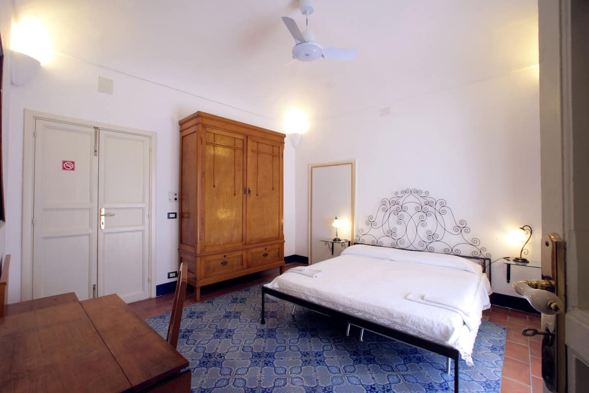 A bedroom with a bed, wooden wardrobe, and a table.