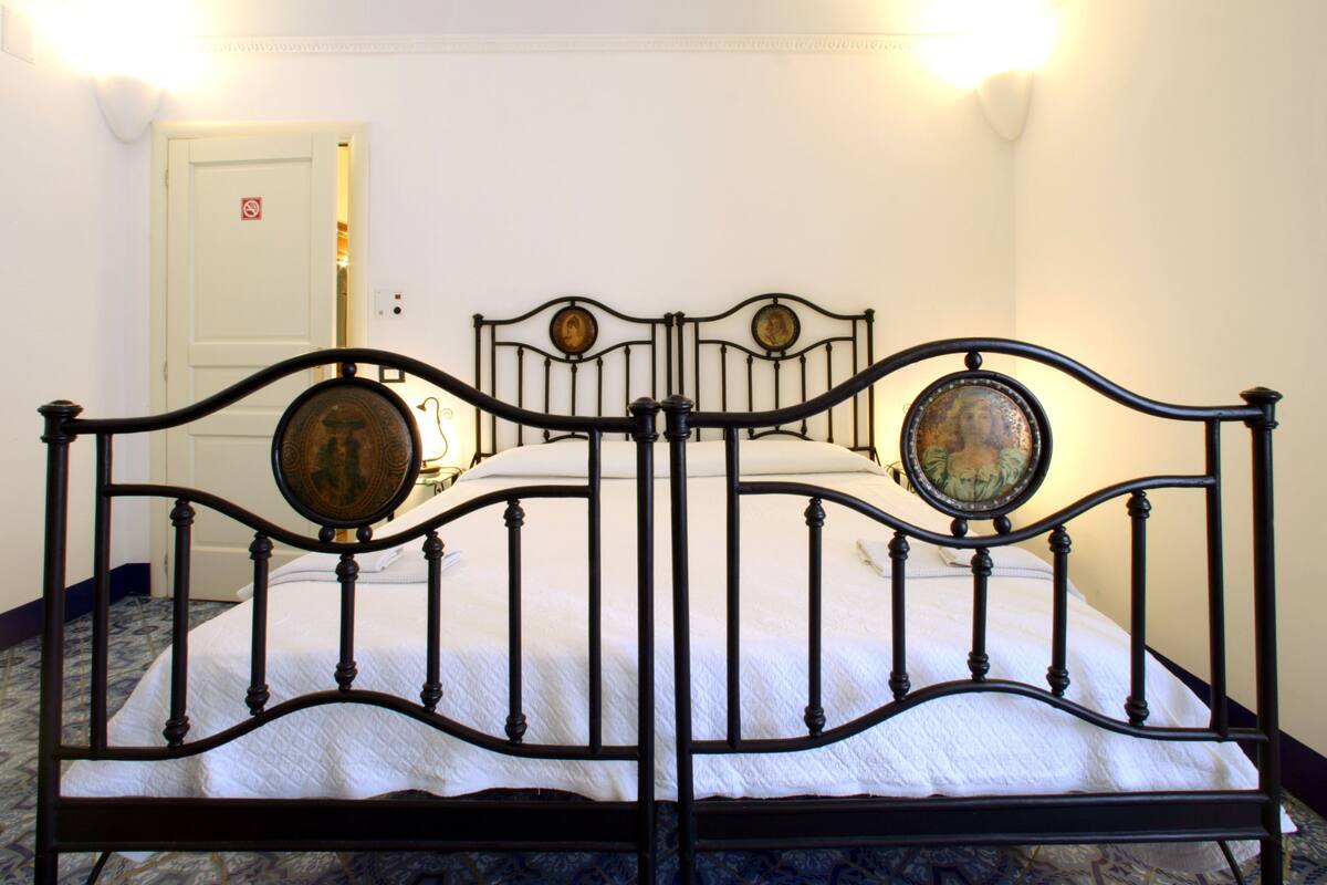 A bed with a metal frame and decorative panels, a white door in the background, and a patterned floor.