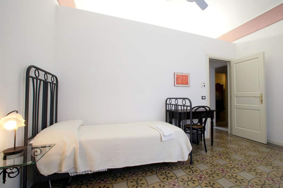 A bedroom with a bed, a chair, a table, and a door.
