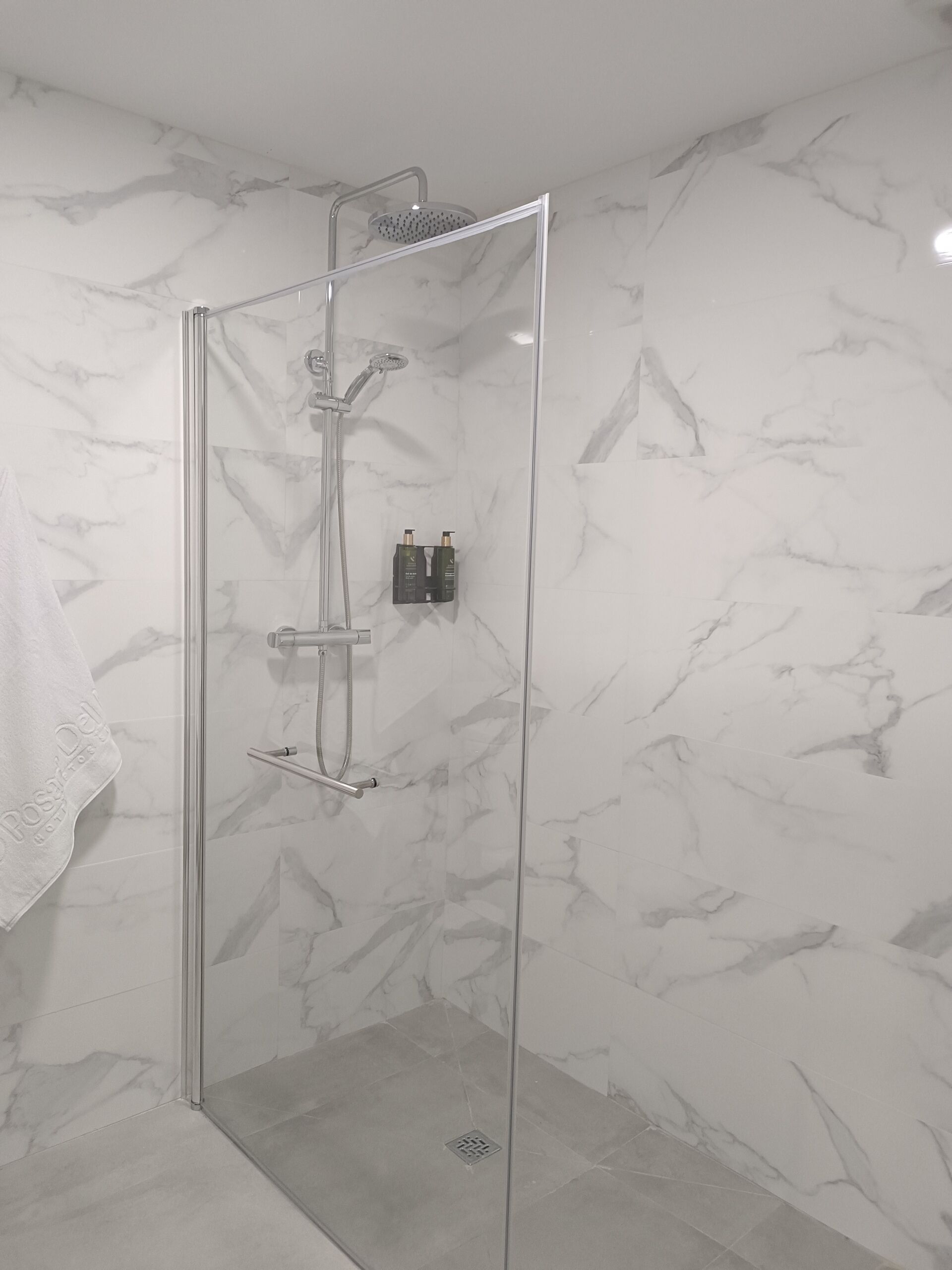 A glass-enclosed shower with a handheld showerhead and a wall-mounted faucet.