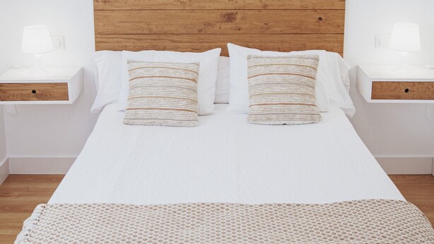 A neatly made bed with a wooden headboard, two bedside tables with lamps, and a patterned throw blanket. - Hotel Posada del Mar (Suances)