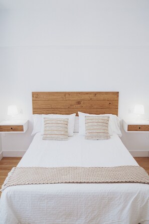 A neatly made bed with a wooden headboard, two bedside tables with lamps, and a patterned throw blanket. - Hotel Posada del Mar (Suances)