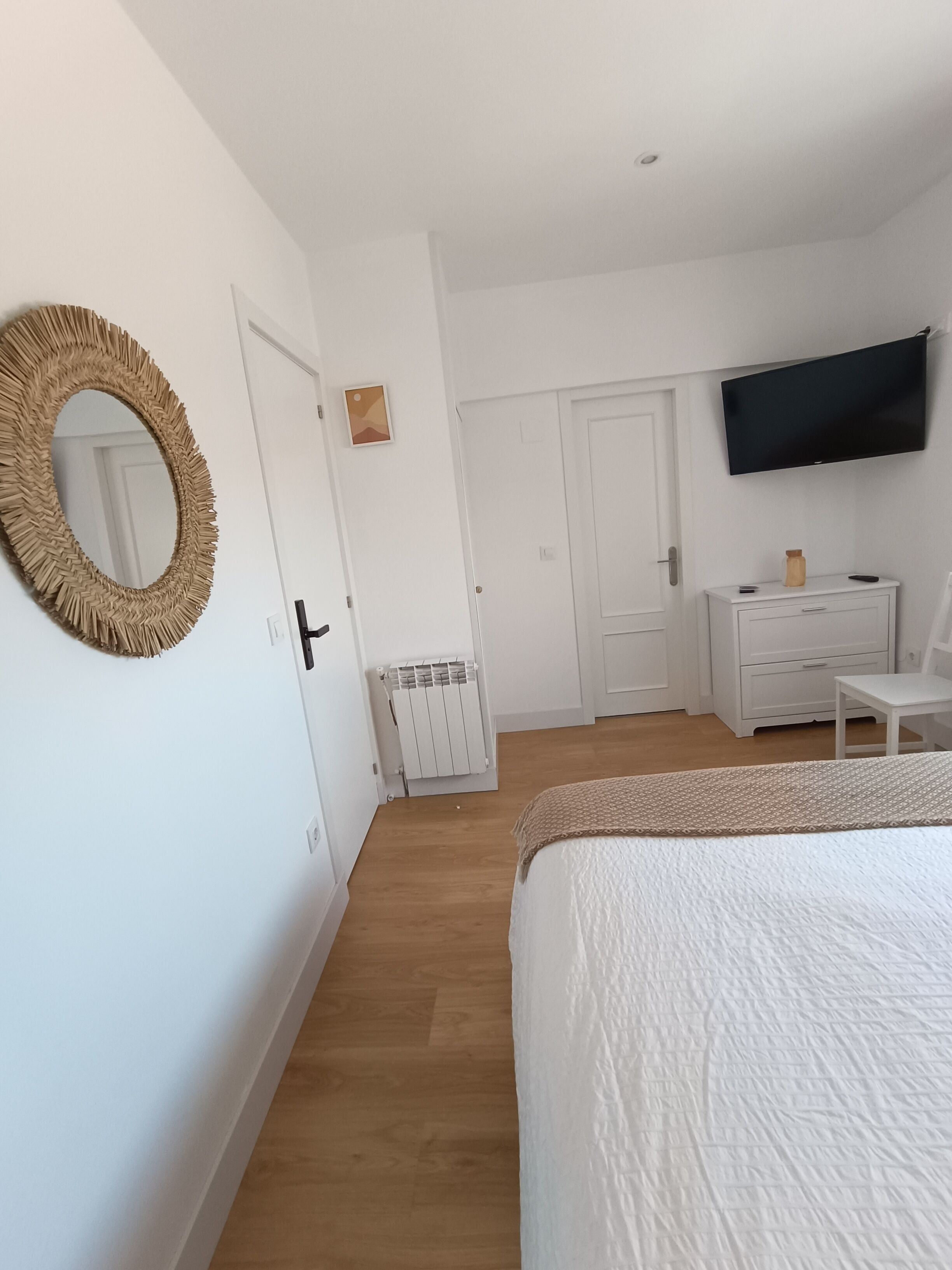 A bedroom with a large bed, a television mounted on the wall, a dresser, and a radiator.