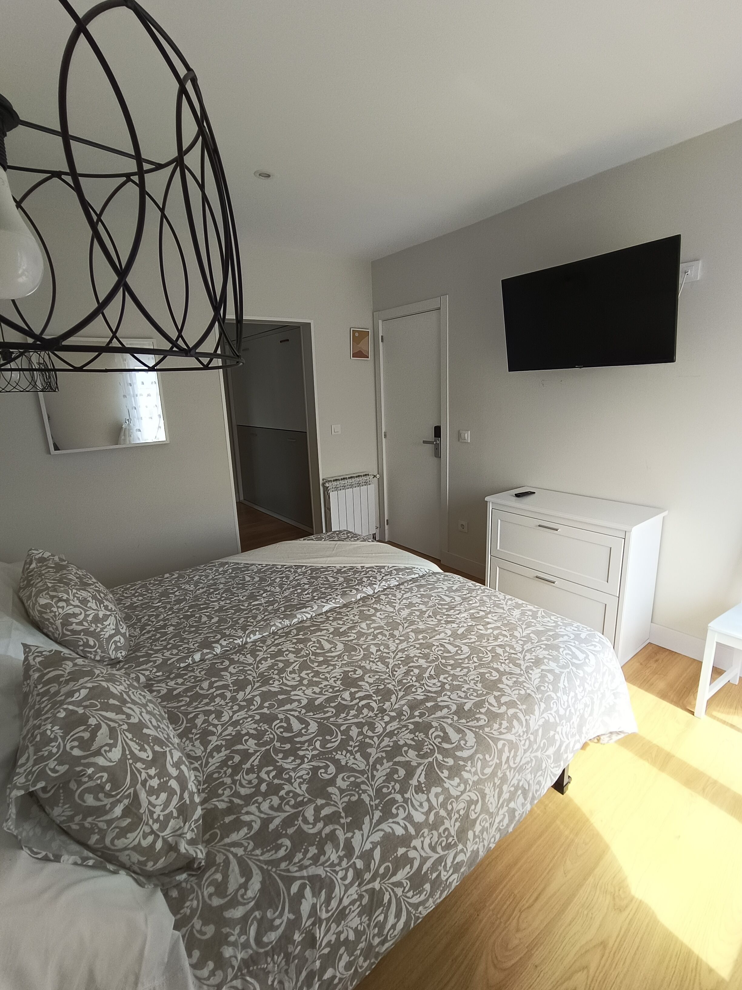 A bedroom with a bed, a dresser, a TV, and a mirror.