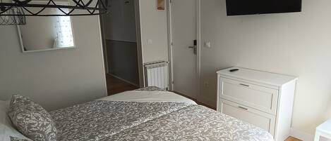 A bedroom with a bed, a dresser, a TV, and a mirror.