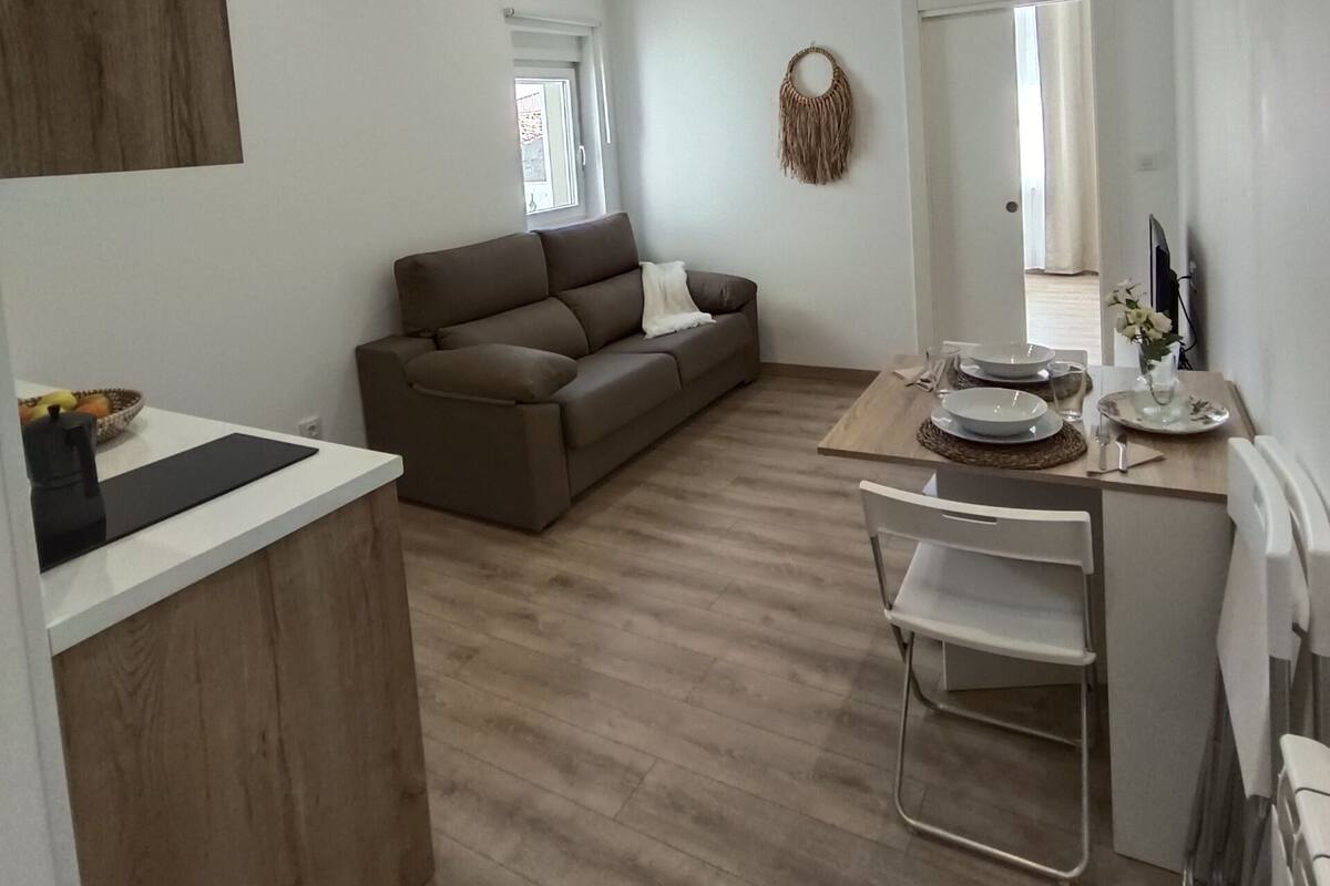 A modern, well-lit living area with a brown sofa, a dining table set with plates and glasses, and a small white chair.