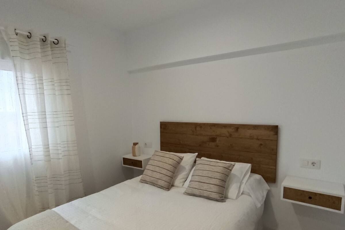 A neatly made bed with a wooden headboard, two bedside tables with lamps, and a bedside shelf.