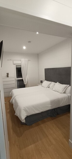 A modern bedroom with a large bed, a bedside table, a window with curtains, and a ceiling light. - Hotel Posada del Mar (Suances)