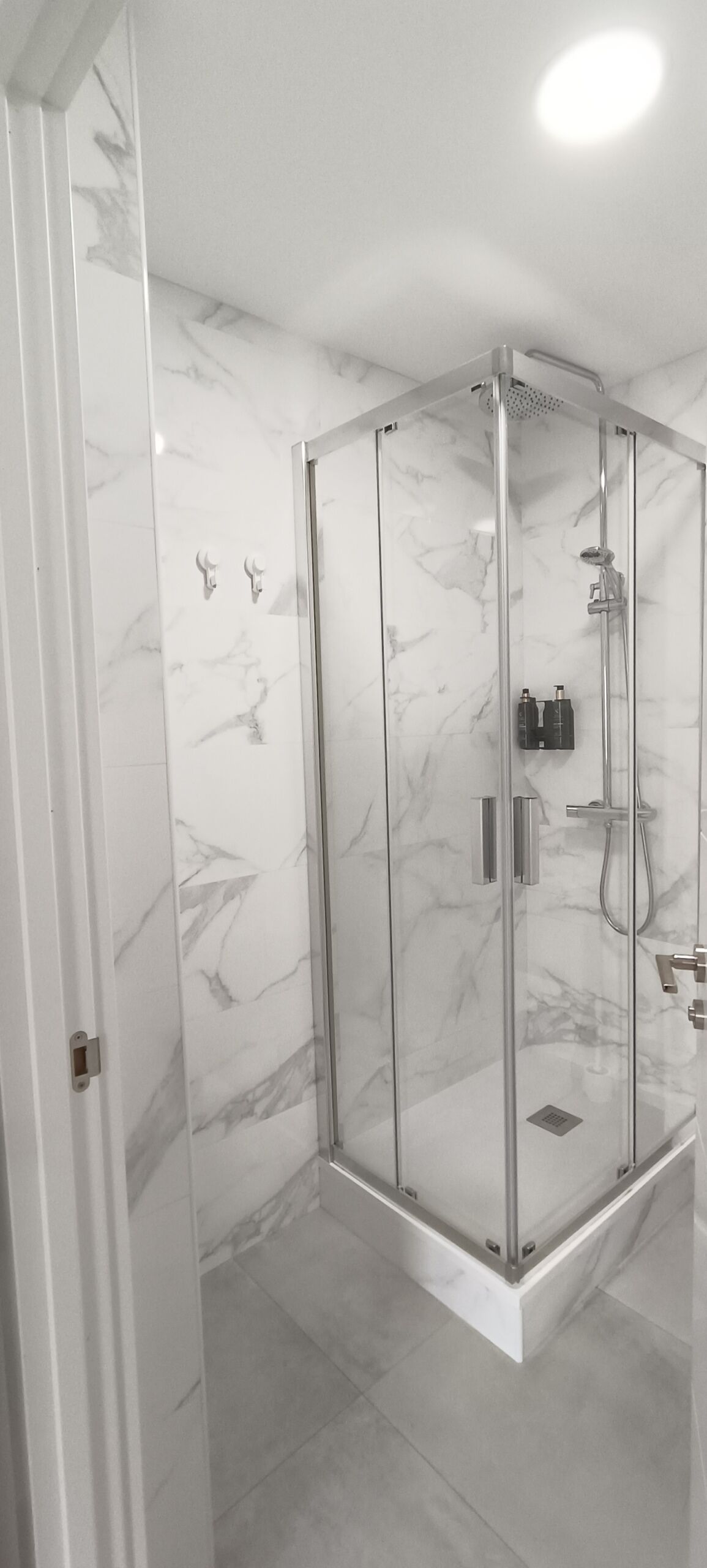 A modern bathroom with a glass-enclosed shower, marble walls, and a tiled floor.