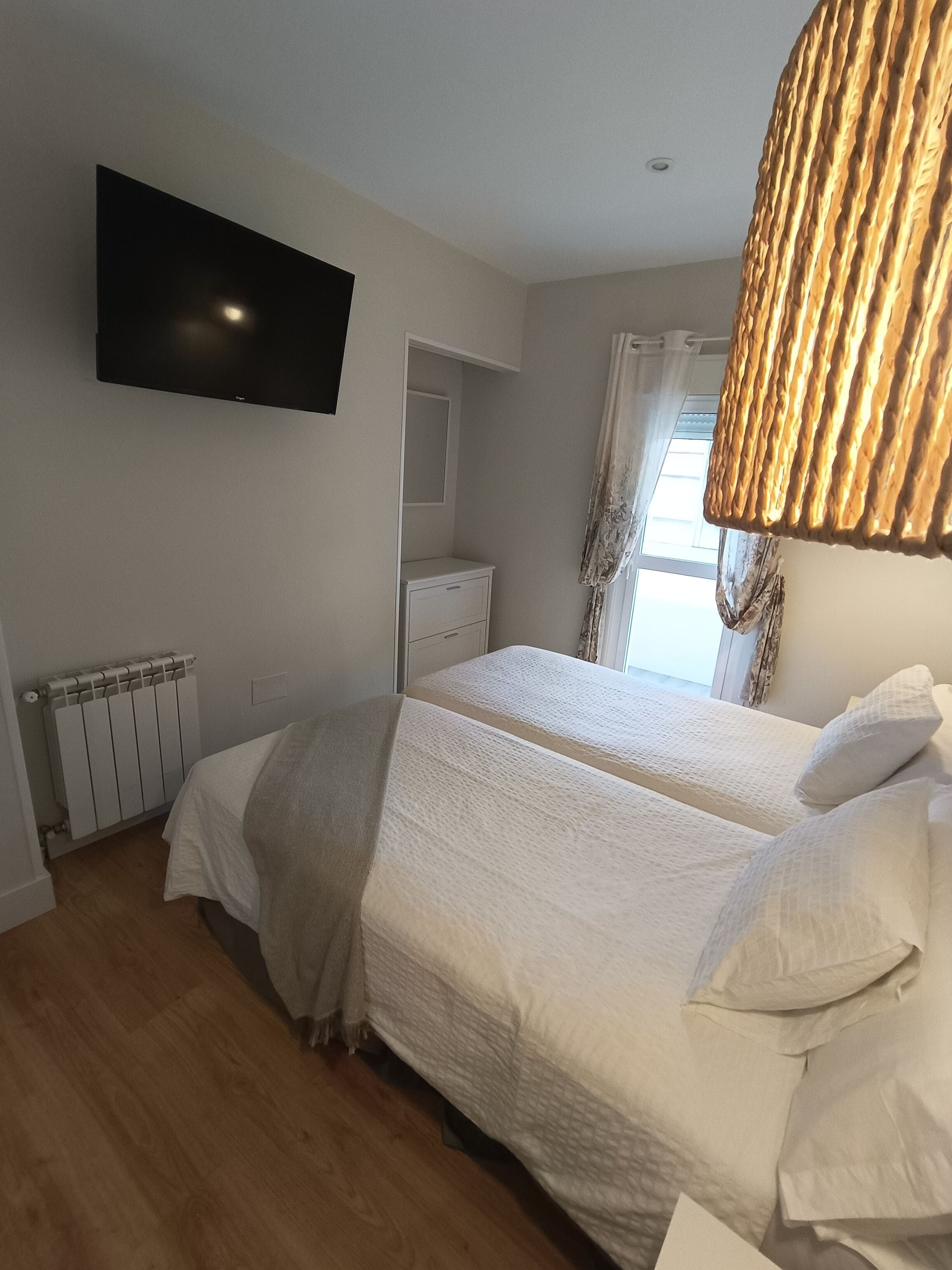 A bedroom with two beds, a flat-screen TV mounted on the wall, a bedside table, and a radiator.