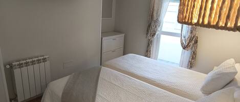 A bedroom with two beds, a flat-screen TV mounted on the wall, a bedside table, and a radiator.