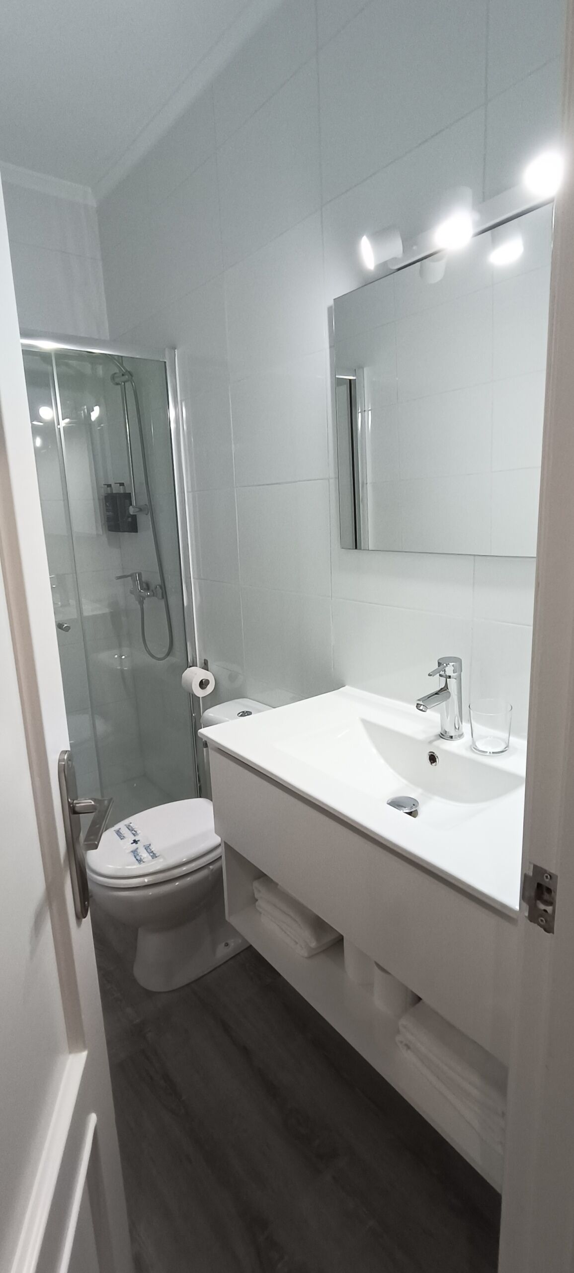 Ein modernes Badezimmer mit einer gläsernen Duschkabine, einem weißen Waschbecken mit Spiegel darüber und einer Toilette mit Deckel.