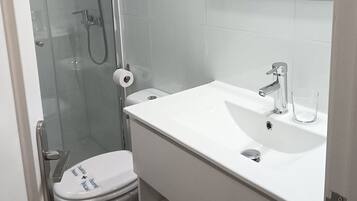 Ein modernes Badezimmer mit einer gläsernen Duschkabine, einem weißen Waschbecken mit Spiegel darüber und einer Toilette mit Deckel.