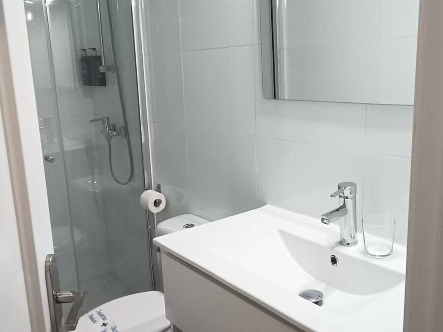 Ein modernes Badezimmer mit einer gläsernen Duschkabine, einem weißen Waschbecken mit Spiegel darüber und einer Toilette mit Deckel.