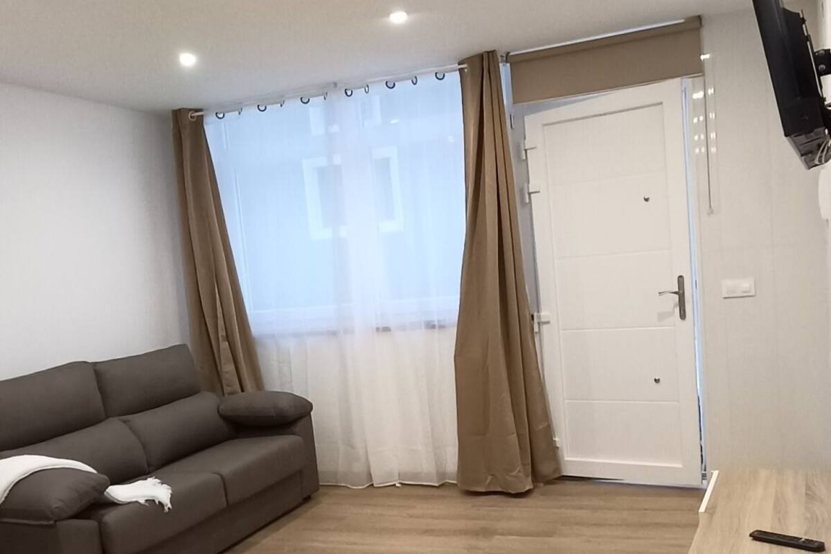 A spacious living room with a brown sofa, a wooden coffee table, and a sliding glass door leading to a balcony.