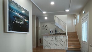 A spacious living area with a wooden staircase, a marble island, and a large painting on the wall. - Hotel Posada del Mar (Suances)