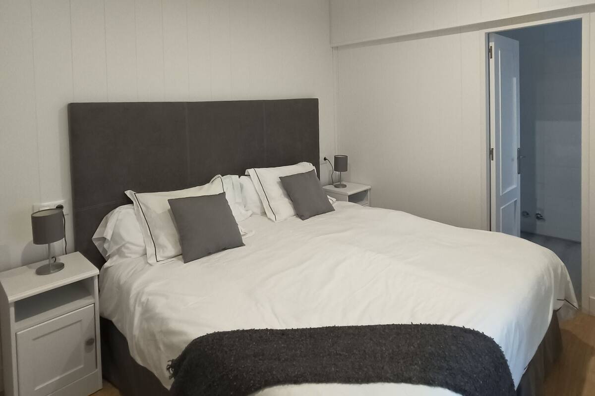 A neatly arranged bedroom with a large bed, bedside tables, and a door leading to another room.