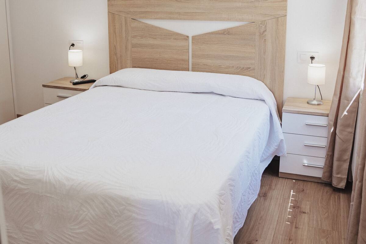 A neatly made bed with a wooden headboard, two bedside tables with lamps, and a wooden floor.