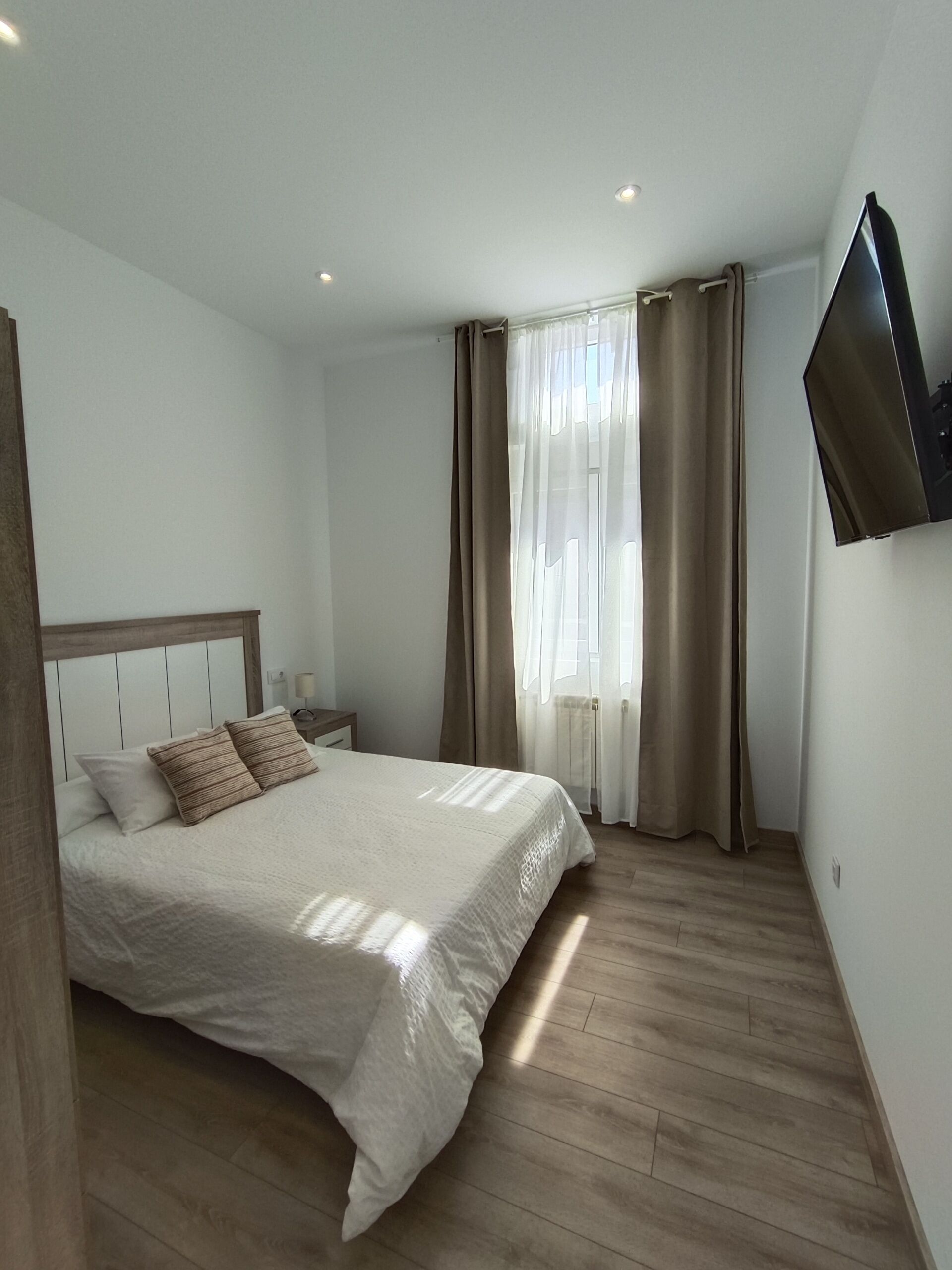 Un dormitorio con cama, cortinas, televisor de pantalla plana y suelo de madera.