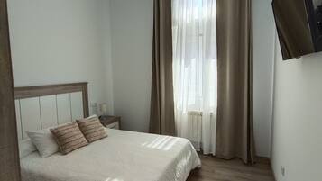 Un dormitorio con cama, cortinas, televisor de pantalla plana y suelo de madera.