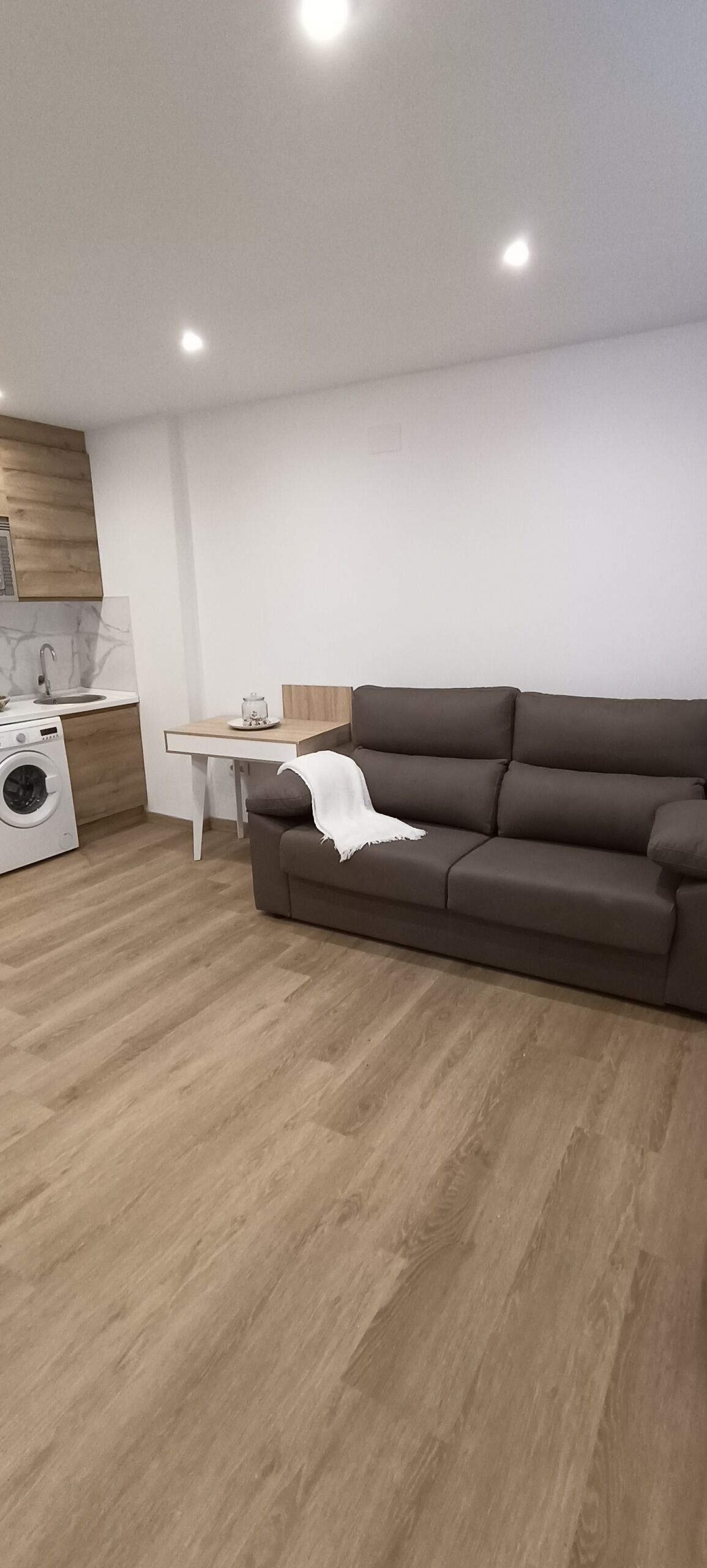 Un salon moderne avec un canapé marron, une petite table et un lave-linge.