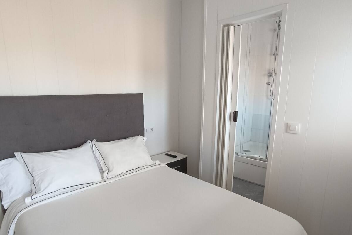 A bedroom with a bed, a nightstand, a door, and a view of the outside.