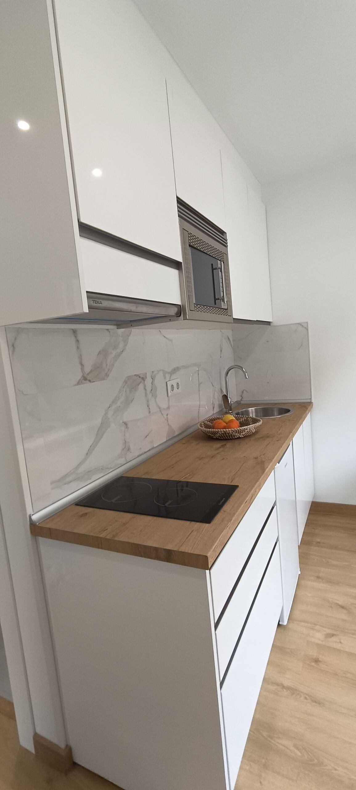 A compact kitchen with white cabinetry, a marble backsplash, a wooden countertop, and a stainless steel sink.