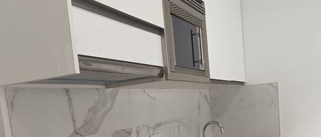 A compact kitchen with white cabinetry, a marble backsplash, a wooden countertop, and a stainless steel sink.